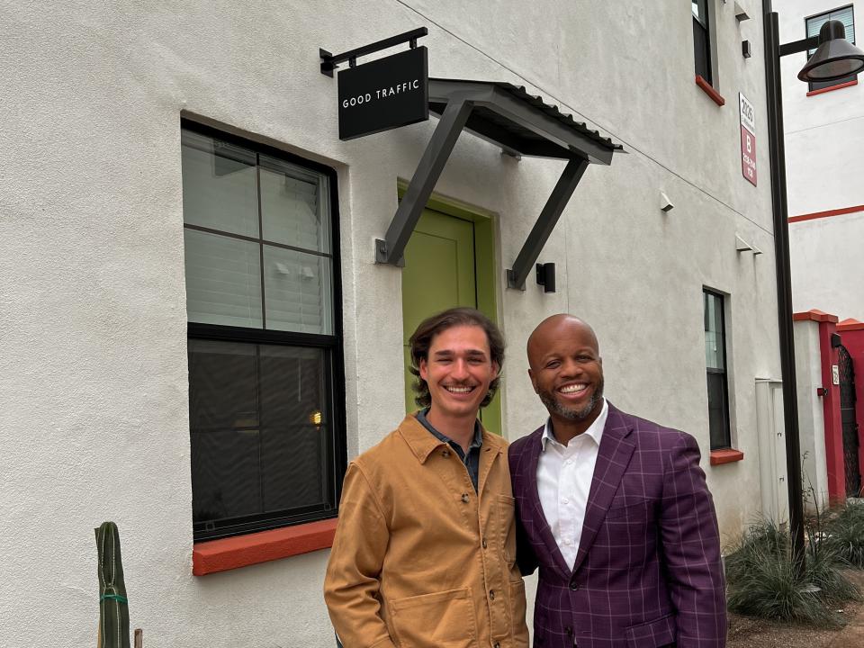 Two men stans in front of a white building smiling