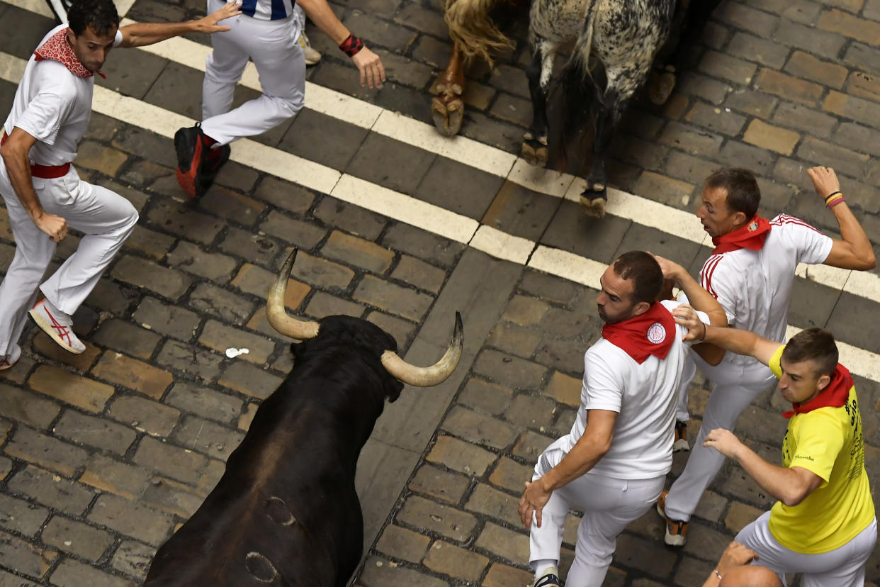 Festival participants look back at a bull as they run down a narrow street.