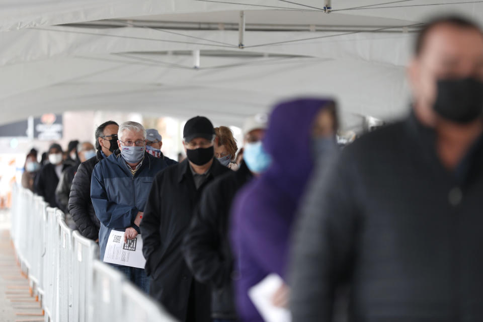 FILE - In this March 10, 2021, file photo, people wait in line at the check-in area to enter the United Center mass COVID-19 vaccination site in Chicago. U.S. deaths from COVID-19 are falling again as the nation recovers from the devastating winter surge. Most forecasts predict coronavirus deaths will fall further in coming weeks, as more people are vaccinated. (AP Photo/Shafkat Anowar, File)