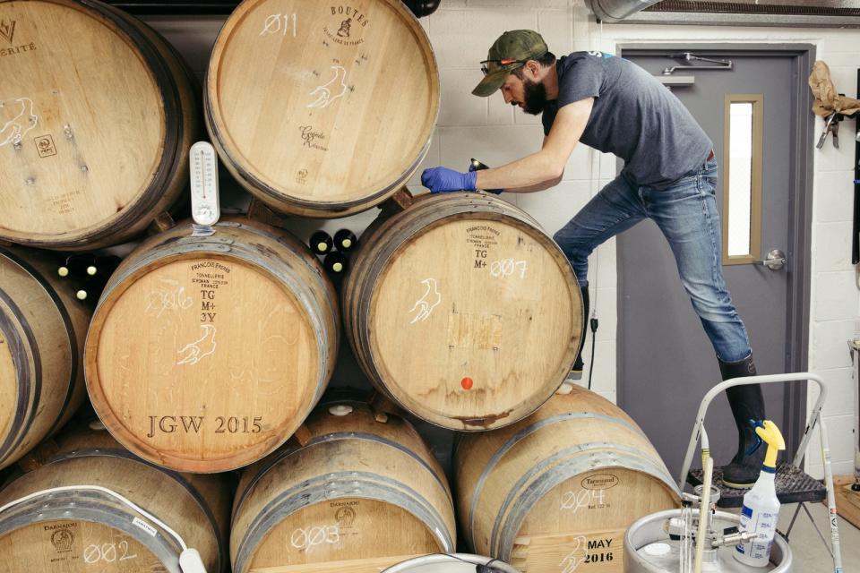 Rob Brennan inspects the fill level for a oak barrel that is used as fermentation and aging vessels for his base wort for different brews.