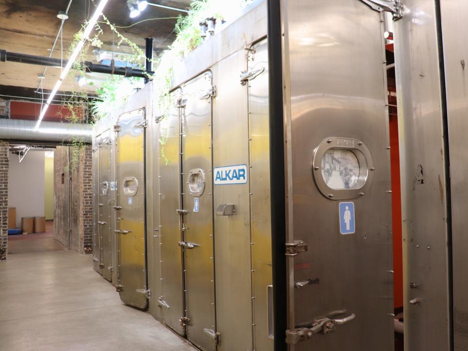 line of stainless steel doors with bathroom signs on them down a hallway with plants in bright light above