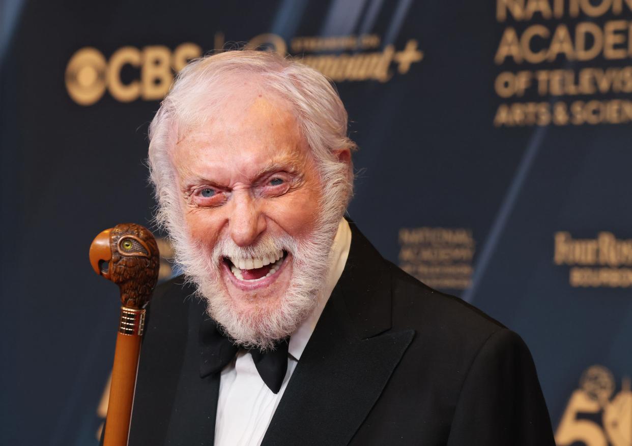 A white man with a beard and holding a walking stick grinning widely for the camera.