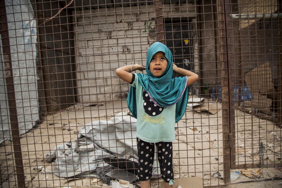 A girl poses for a photograph as she stands in front of one of the closed shops at al-Hol camp that houses some 60,000 refugees, including families and supporters of the Islamic State group, many of them foreign nationals, in Hasakeh province, Syria, Saturday, May 1, 2021. Kurdish officials say security has improved at the sprawling camp in northeast Syria, but concerns are growing of a coronavirus outbreak in the facility. (AP Photo/Baderkhan Ahmad)