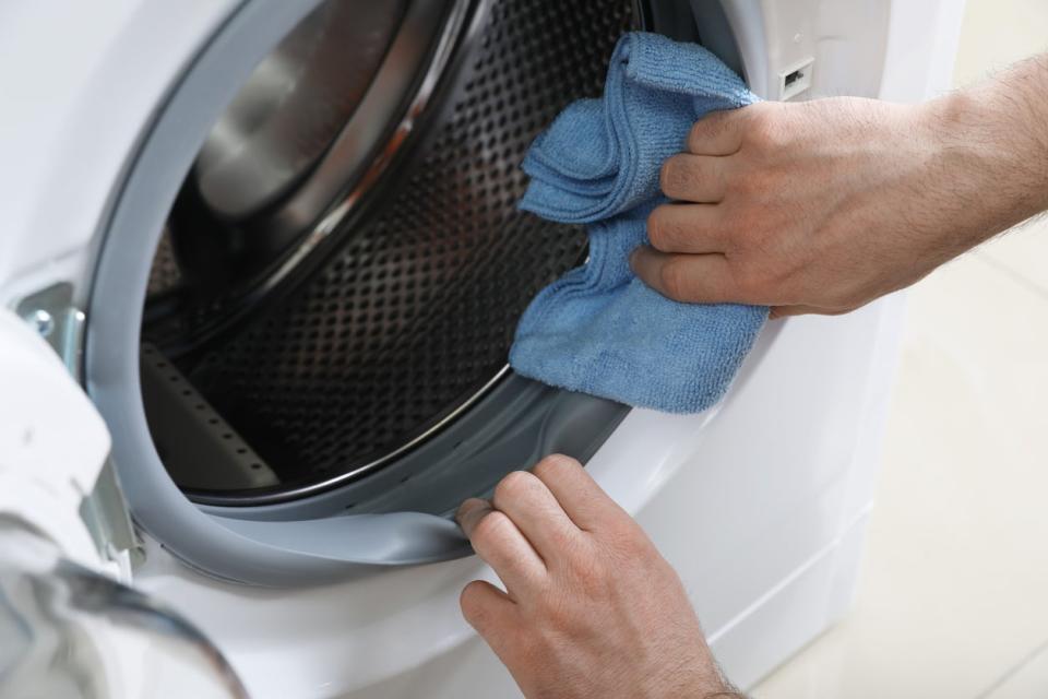 Man cleaning empty washing machine with rag