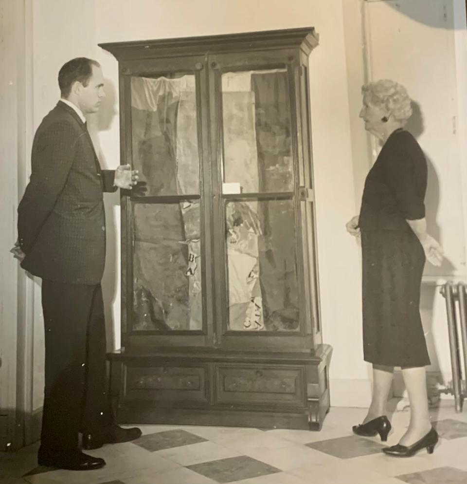 Jerry Stephens stands with an unidentified member of the Daughters of the Texas Republic as they discuss a Mexican battle flag found in the attic of the old Texas Land Office, once a Confederate museum, now the Capitol Visitors Center. On the back of the print, the photo is credited to Blair E. Wilkins and is dated March. 12, 1965.