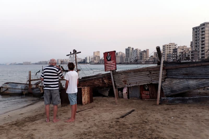 FILE PHOTO: People gaze at Varosha, a former resort area fenced off by the Turkish military since the 1974 division of Cyprus, as they walk on a beach in Famagusta