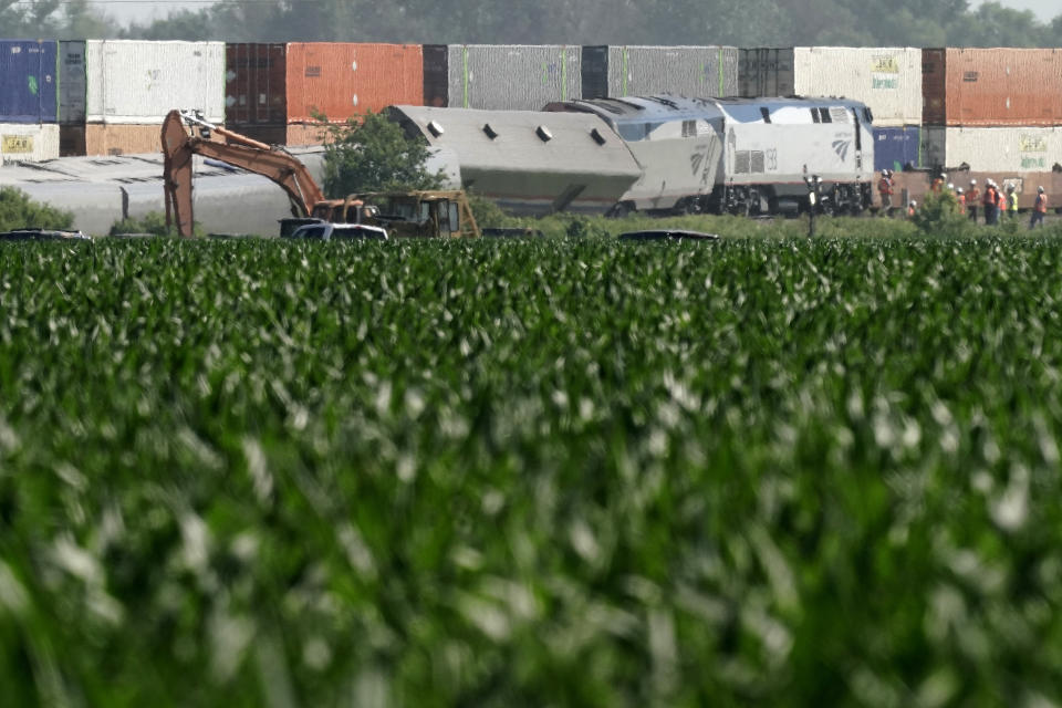 A freight train passes along side a derailed Amtrak train Tuesday, June 28, 2022, near Mendon, Mo. The train derailed after hitting a dump truck Monday killing the truck driver and others on the train and injuring several dozen other passengers on the Chicago-bound train. (AP Photo/Charlie Riedel)