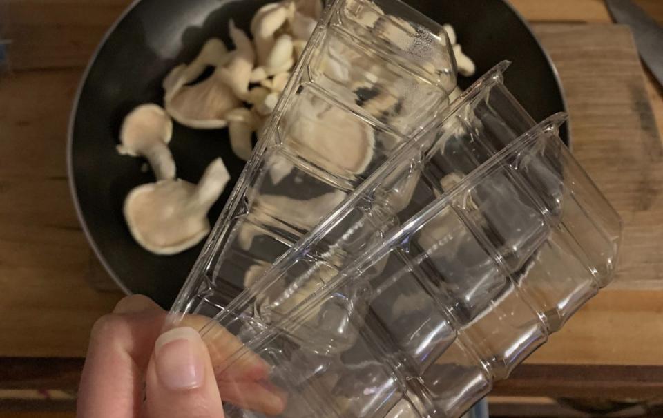 A woman displays the three plastic punnets used to package some oyster mushrooms from Woolworths