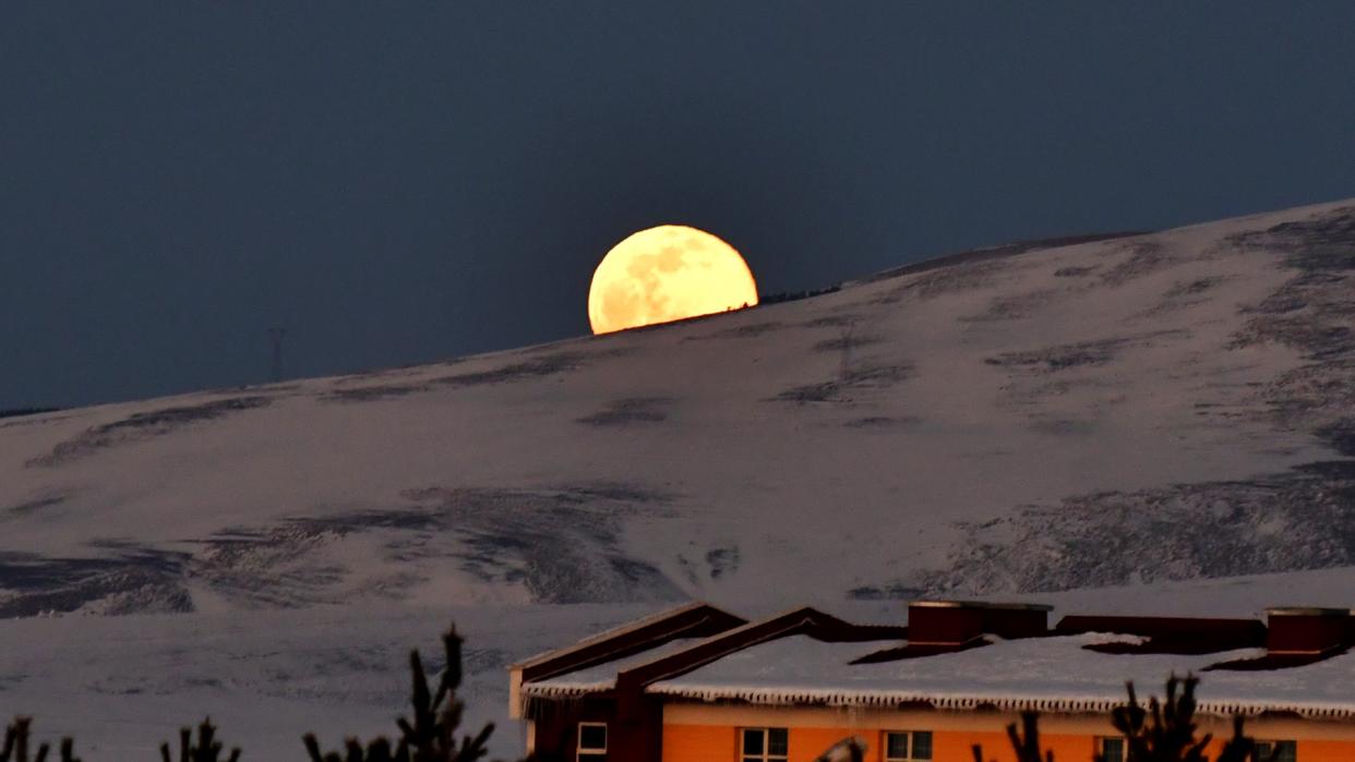  A bright full moon rises behind a snow-covered mountain. 