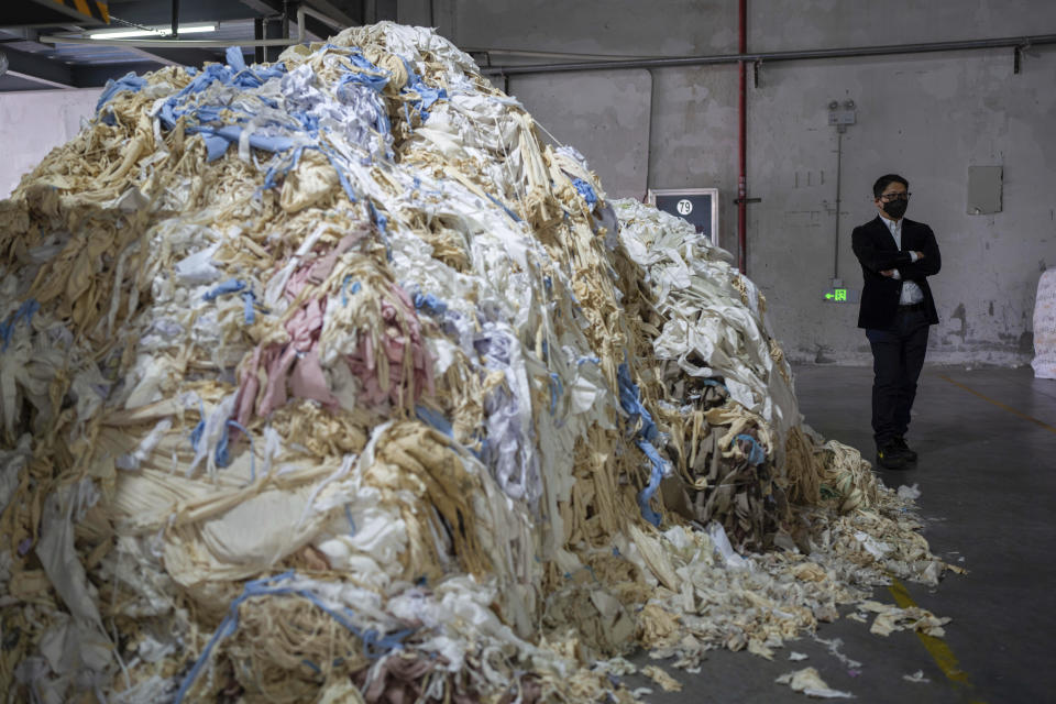 Kowen Tang, sales director of the Wenzhou Tiancheng Textile Company, one of China's largest cotton recycling plants, stands near a mound of discarded textiles in Wenzhou in eastern China's Zhejiang province on March 20, 2024. (AP Photo/Ng Han Guan)