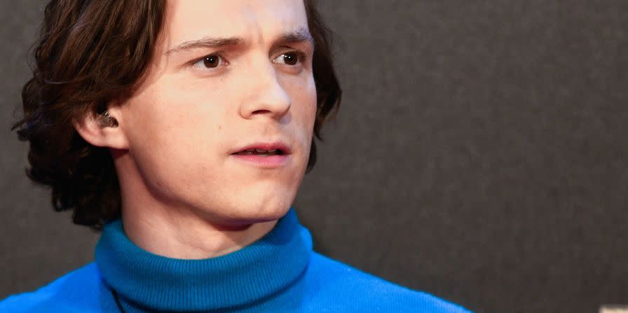 tom holland, wearing a blue turtleneck shirt, looks off camera