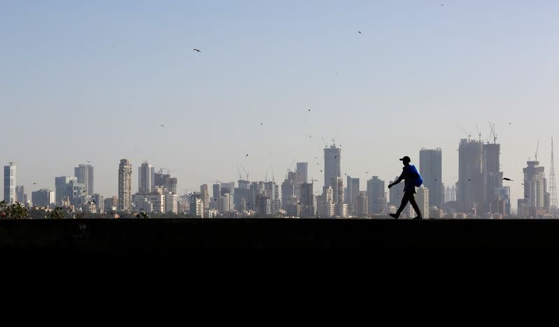 FILE PHOTO: A man walks along a wall overlooking the central Mumbai's financial district skyline