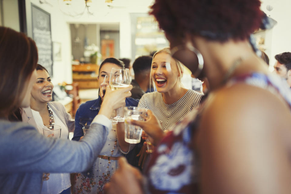 A group of women celebrate by toasting with glasses of wine at a bar.