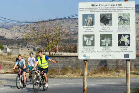 Environmental activists on bicycles pass by a billboard showing the bio-diversity of Cijevna river, during a protest near the river's dried out riverbed in Dinosa village, near Tuzi, Montenegro October 20, 2018. REUTERS/Stevo Vasiljevic