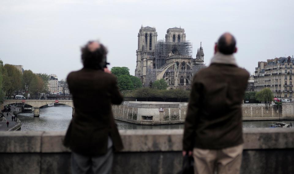 People stop to see and photograph the Notre Dame cathedral after the fire in Paris, Tuesday, April 16, 2019. Experts are assessing the blackened shell of Paris' iconic Notre Dame cathedral to establish next steps to save what remains after a devastating fire destroyed much of the almost 900-year-old building. With the fire that broke out Monday evening and quickly consumed the cathedral now under control, attention is turning to ensuring the structural integrity of the remaining building.