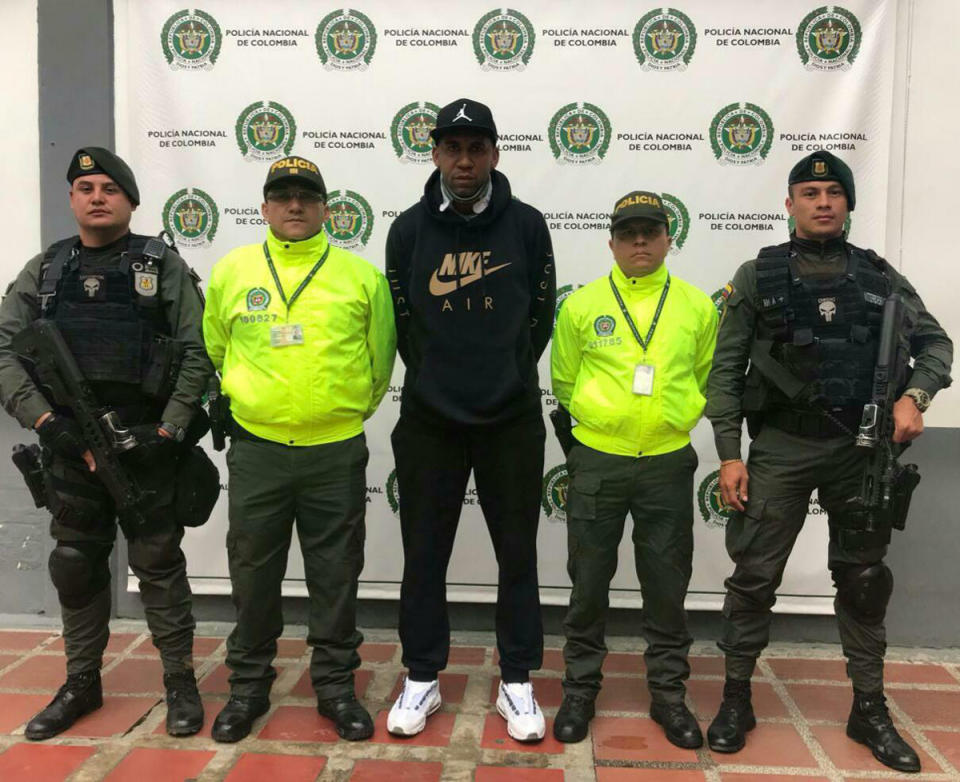 In this handout photo released by Colombia's National Police, former Southampton and Portsmouth soccer player Jhon Viafara stands flanked by police officers after his arrest on a U.S. drug warrant, in Jamundi, Colombia, Tuesday, March 19, 2019. Colombia's chief prosecutor's office said that prosecutors in Texas believe the midfielder was part of a criminal network tied to the nation's Gulf drug cartel, which for a decade moved large shipments of cocaine into the U.S. (Colombia's National Police via AP)