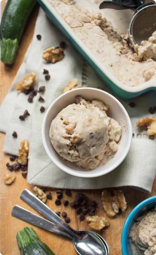 Scoop of ice cream in a white bowl on a placemat on a wooden board next to spoons