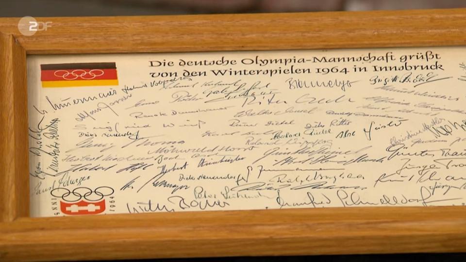 <p>Deutschmanek zeigte die einzelnen Teile: Teilnehmermedaille, Heft, Startnummern, Kofferkarte, Anstecknadel, Mantel und die Unterschriften des gesamten deutschen Olympia-Teams mit Namen wie Willy Bogner, Georg Thoma, Marika Kilius und Hans-Jürgen Bäumler. (Bild: ZDF)</p> 