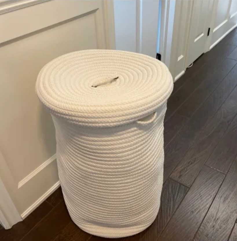 Reviewer's photo of the woven laundry hamper in the color white with lid in a home setting