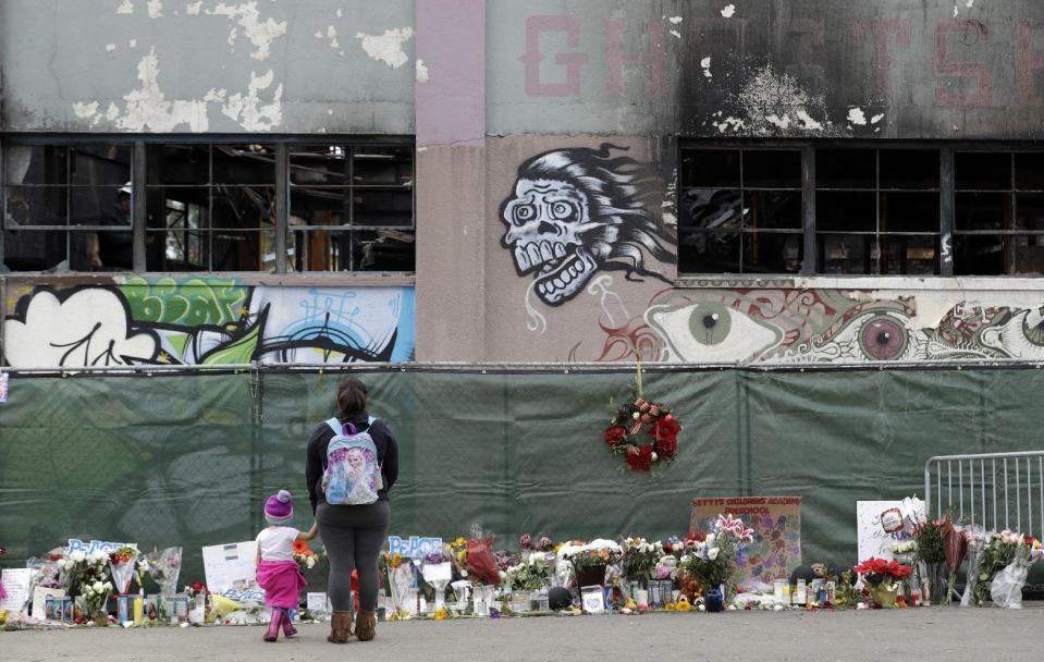 Flowers, pictures, signs and candles, are placed at the scene of a warehouse fire Tuesday, Dec. 13, 2016, in Oakland , Calif. The fire killed dozens of people during a electronic dance party as it raced through the building, in the deadliest structure fire in the U.S. in more than a decade. (AP Photo/Marcio Jose Sanchez)