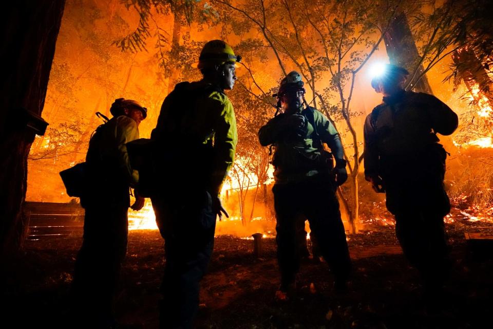 Firefighters stand near a blaze in Boulder Creek (AP)