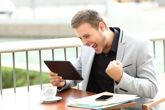 A young man, tablet in hand, celebrates good news with a fist pump