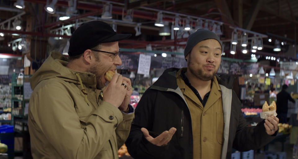 This image released by Netflix shows host David Chang, right, and actor Seth Rogen eating donuts at Lee's Donuts in Vancouver, Canada, in a scene from the Netflix series, "Breakfast, Lunch & Dinner." (Netflix via AP)