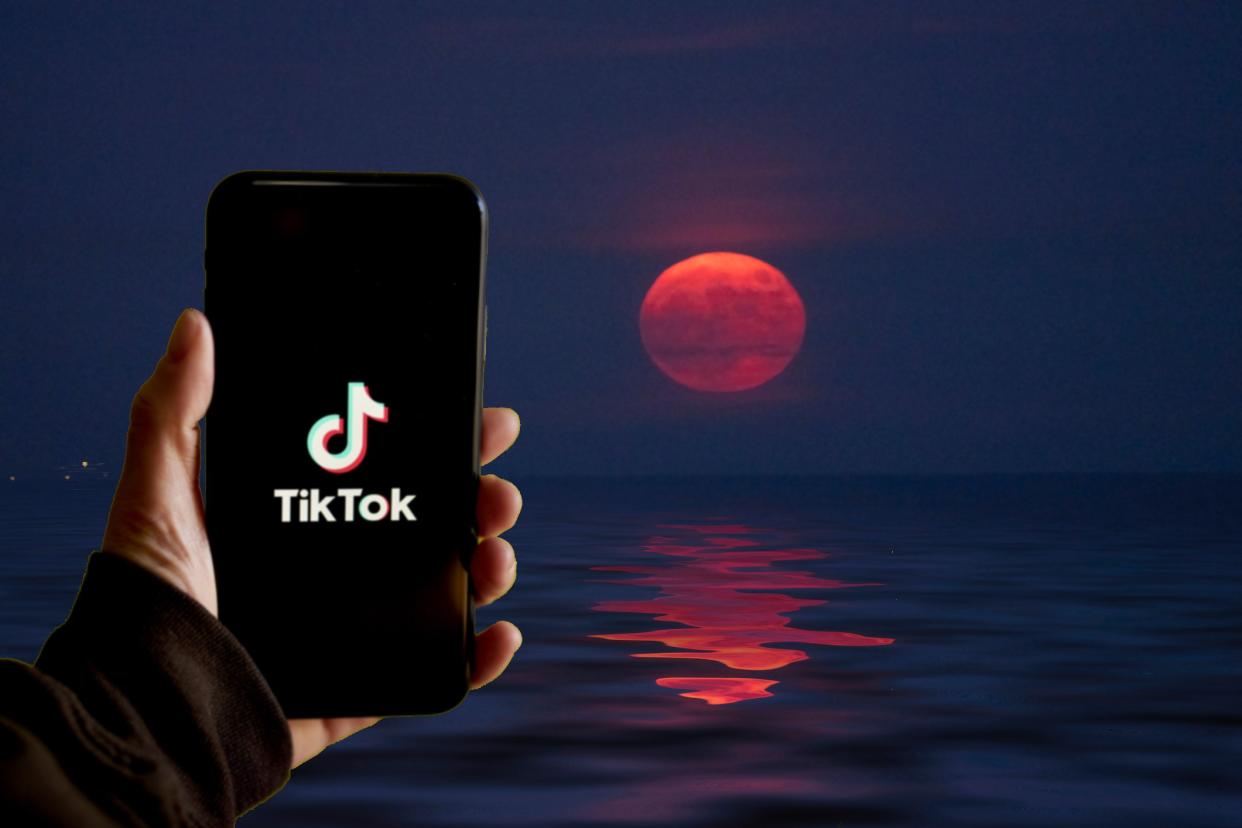  a hand holding up a phone using TikTok with the full moon in the background 