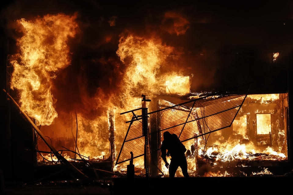 FILE - In this Saturday, May 30, 2020 file photo, a protester adds materials to a fire of a building that once housed a check cashing business, in St. Paul, Minn. The destruction caused by vandals and looters in cities across the country, who struck as demonstrators took to the streets in reaction to the killing of George Floyd in Minneapolis, has devastated small businesses already reeling from the coronavirus outbreak. (AP Photo/John Minchillo)