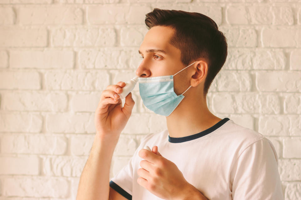 Portrait of young sick man using nasal drops for runny congested nose. Confident sick doctor in medical protective mask on face using nose spray. Pandemic coronavirus COVID-19 nCov-19 symptoms