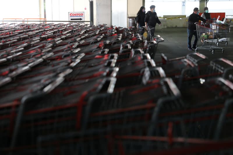 Shoppers wearing protective face masks walk past a shopping cart corral outside of a Costco store in Wheaton, Maryland