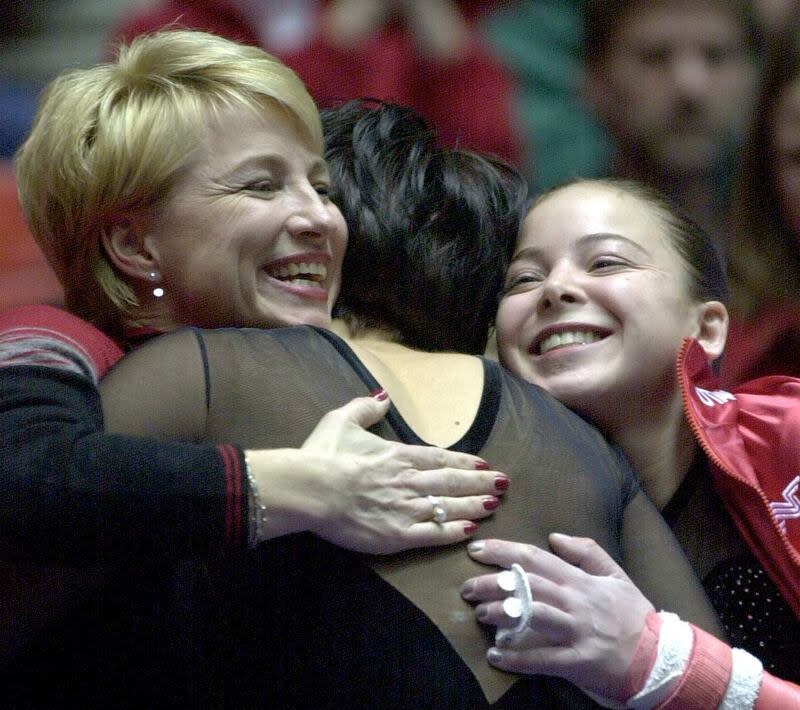 Theresa Kulikowski gets a hug from coach Megan Marsden and teammate Deidra Grahm after her bars routine.