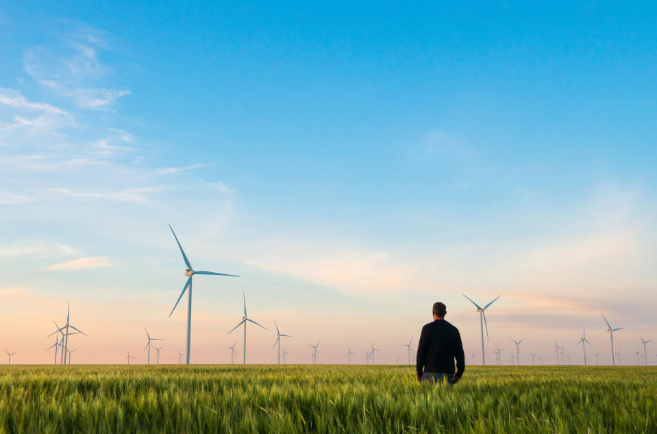 A man in a green field with wind turbines in the background.