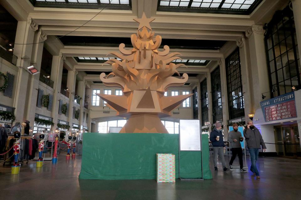 People walk past "The Giving Tree," a 17-foot cardboard Christmas Tree in the Grand Arcade in the Asbury Park Boardwalk by Mike "Porkchop" La Vallee and Bradley Hoffer is shown Wednesday, December 1, 2021.  The art project is presented by the community arts non-profit the Wooden Walls Project and the Asbury Park Boardwalk.