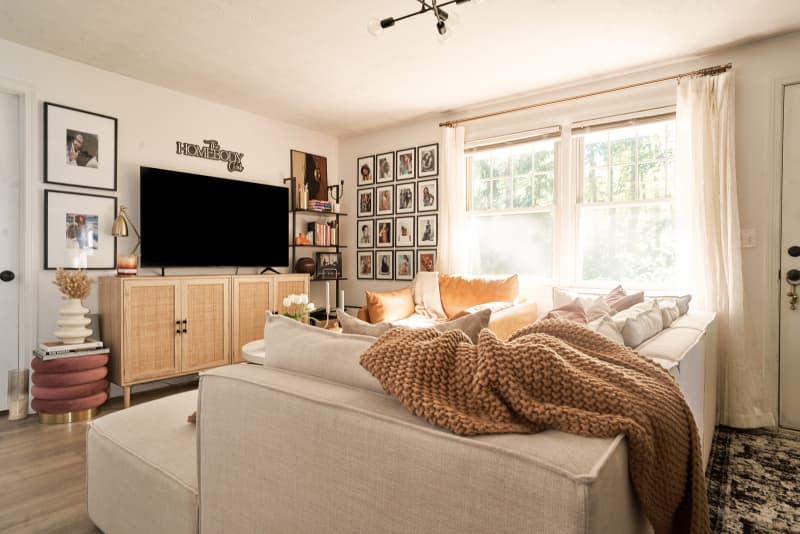 living room with large off-white sectional sofa with peach and warm hued pillows and throw, grid-style gallery wall