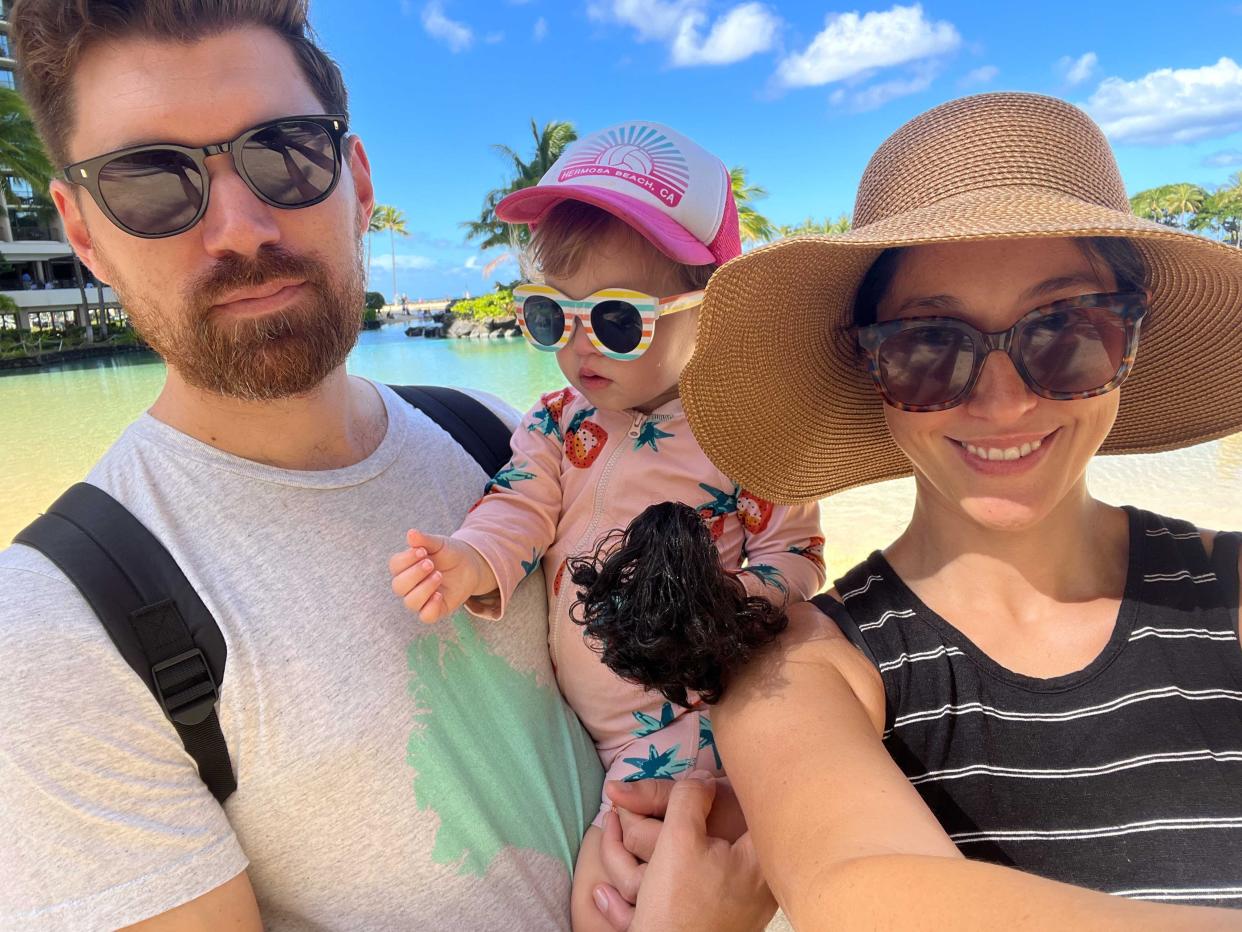 A family of three posing for a selfie all wearing sunglasses in a tropical location.