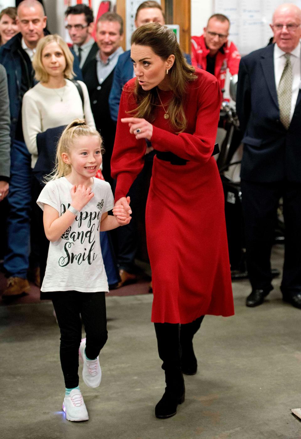 Kate Middleton wears a red Zara dress while holding a child's hand and pointing.
