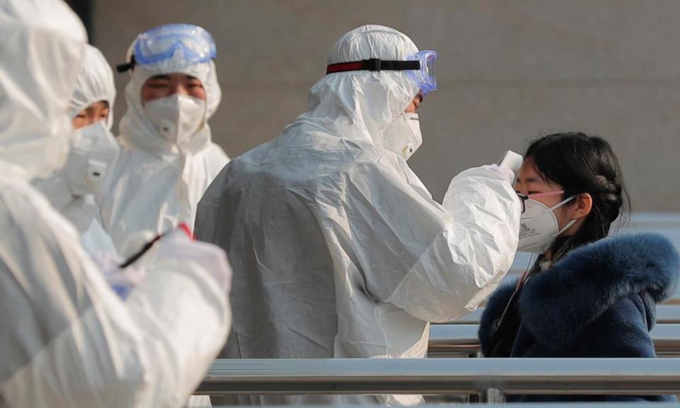 Security personnel wearing hazardous material suits measure body temperatures of passengers at the entrance of a subway station in Beijing.