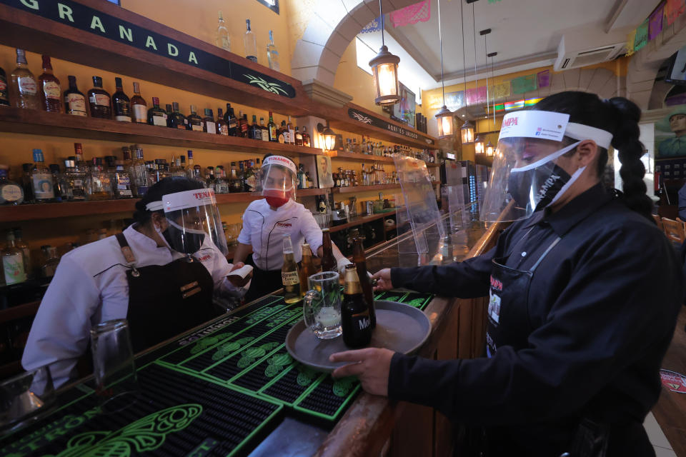 MEXICO CITY, MEXICO - AUGUST 22: A waiter wearing protective gear to follow sanitary protocols against Covid-19 takes a drink order to a customer table during a working day at Salon Tenampa on August 22, 2020 in Mexico City, Mexico. After more than three months of a lockdown ordered by the local and Federal Governments to halt the spread of Coronavirus (Covid-19) the Salon Tenampa, as many other traditional restaurants and Cantinas in Mexico City, faces a complicated situation as it can only operate at 30% of its full capacity. The venue must follow strict and meticulous sanitary protocols for restaurants ordered by the authorities. (Photo by Hector Vivas/Getty Images)