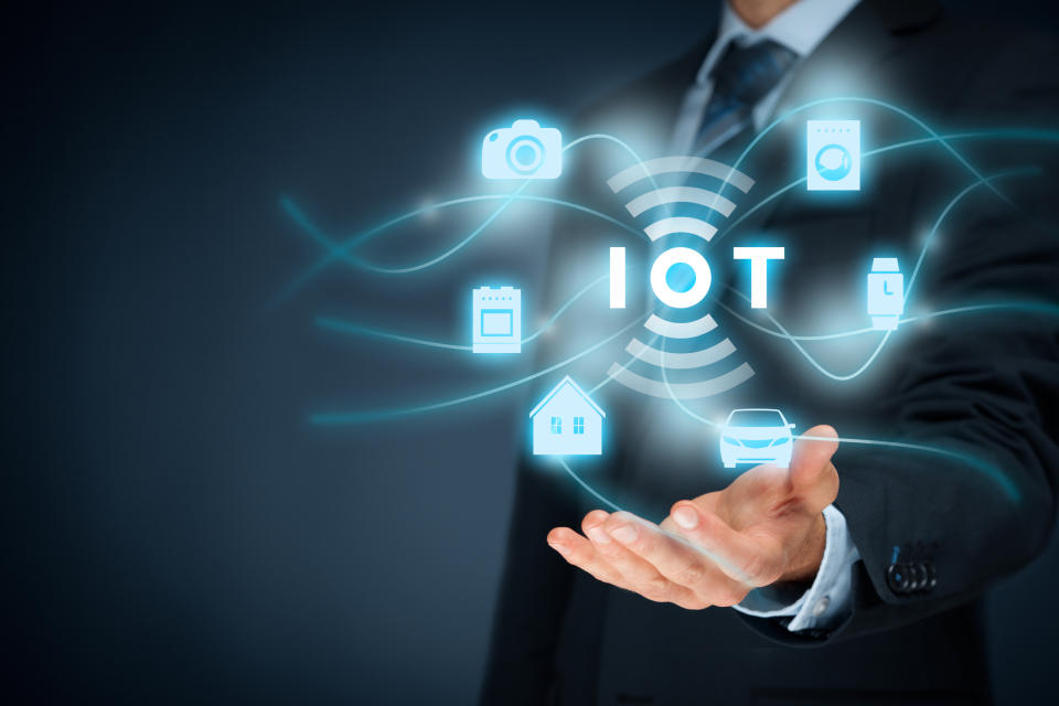 A man extending a hand above float icons for different IoT applications and the letters "IOT"