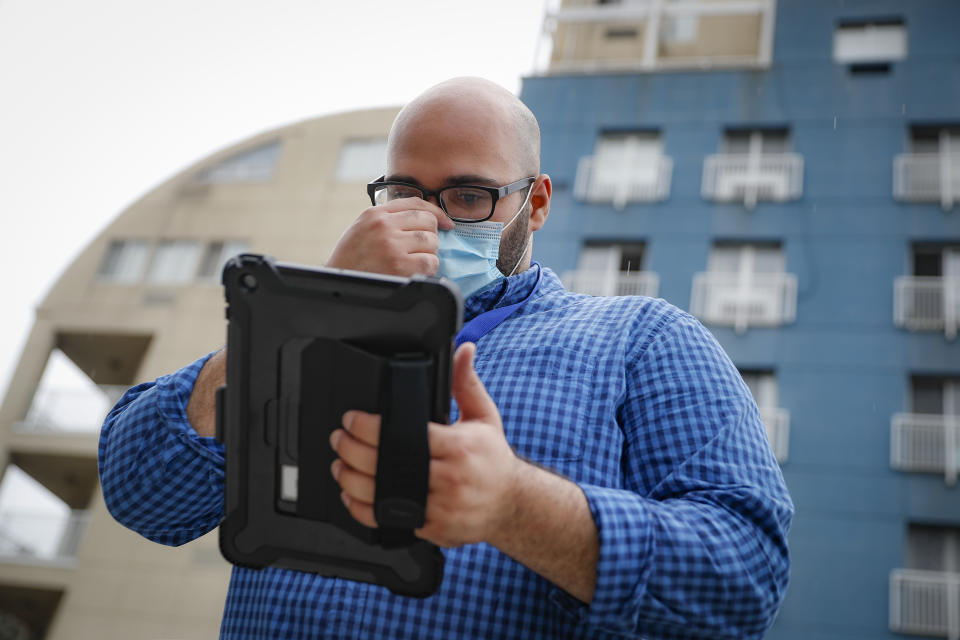 Joseph Ortiz, a contact tracer with New York City's Health + Hospitals battling the coronavirus pandemic, uses his tablet to gather information as he heads to a potential patient's home Thursday, Aug. 6, 2020, in New York. The city has hired more than 3,000 tracers and the city says it's now meeting its goal of reaching about 90% of all newly diagnosed people and completing interviews with 75%. (AP Photo/John Minchillo)