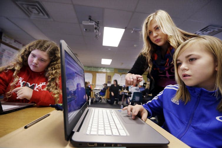 A computer science teacher, center, helps fifth grade students learn programming. AP Photo/Elaine Thompson