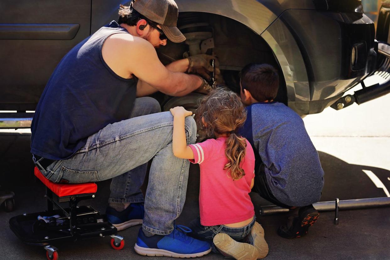 a young boy and girl are watching their father work on a car.