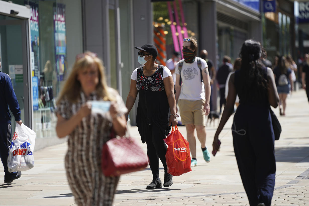 People walk wearing face masks to try to stop the spread of coronavirus in a shopping area in Manchester, northern England, Friday, July 31, 2020. The British government on Thursday night announced new rules on gatherings in some parts of Northern England, including Manchester, that people there should not mix with other households in private homes or gardens in response to an increase trend in the number of cases of coronavirus cases per 100,000 people. (AP Photo/Jon Super)