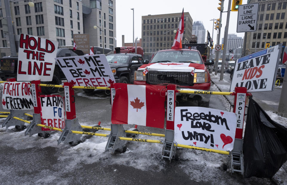 Signs sit on a barricade in front of parked vehicles as part of the trucker protest, Tuesday, Feb. 8, 2022 in Ottawa's downtown core. Canadian lawmakers expressed increasing worry about protests over vaccine mandates other other COVID restrictions after the busiest border crossing between the U.S. and Canada became partially blocked. (Adrian Wyld /The Canadian Press via AP)