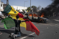 A demonstrator holds a Senegalese flag as he kneels in front of a burning car during protests against the arrest of opposition leader and former presidential candidate Ousmane Sonko, Senegal, Monday, March 8, 2021. Senegalese authorities have freed opposition leader Ousmane Sonko while he awaits trial on charges of rape and making death threats. The case already has sparked deadly protests threatening to erode Senegal's reputation as one of West Africa’s most stable democracies. That's because Sonko's supporters are accusing President Macky Sall of pursuing the criminal charges to derail the opposition figure's prospects in the upcoming 2024 election. (AP Photo/Leo Correa)
