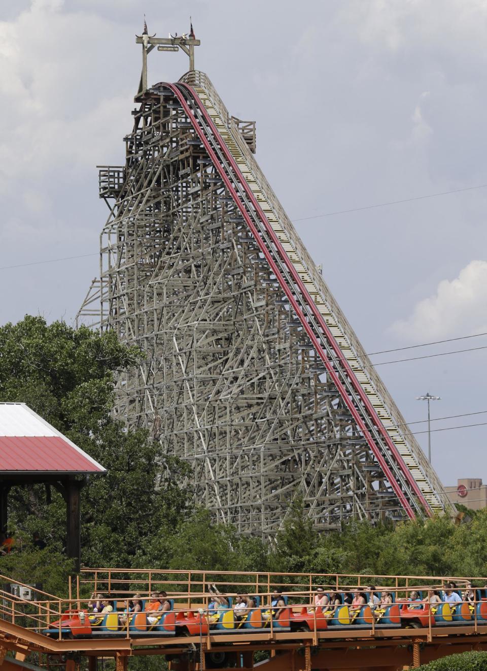 The Texas Giant roller coaster ride sits idle in the background as people take in another roller coaster ride at the Six Flags Over Texas park Saturday, July 20, 2013, in Arlington, Texas. Investigators will try to determine if a woman who died while riding the roller coaster at the amusement park Friday night fell from the ride after some witnesses said she wasn't properly secured.(AP Photo/LM Otero )