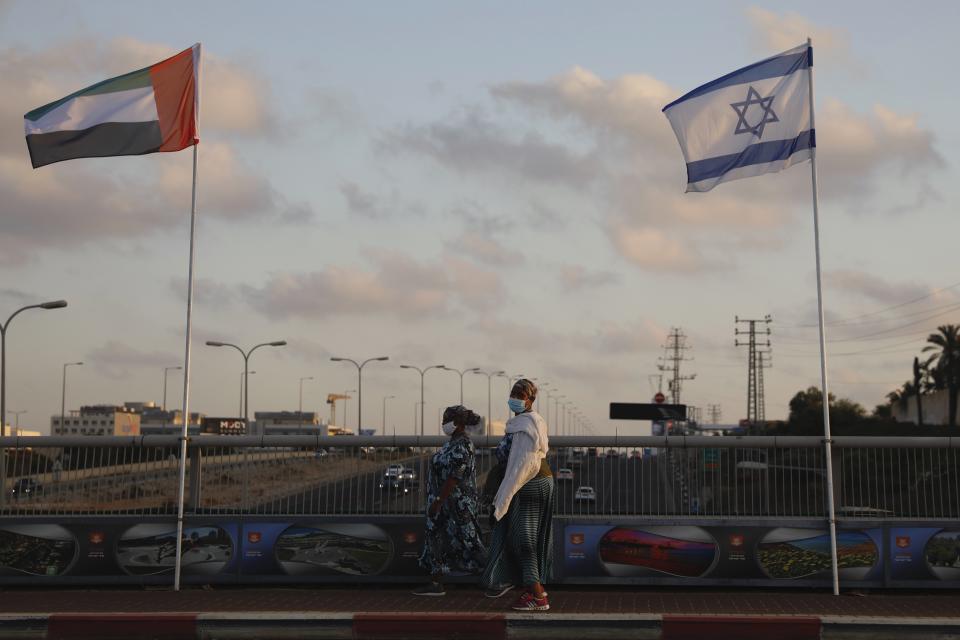 Women wearing face masks against the coronavirus walk past United Arab Emirates and Israeli flags at the Peace Bridge in Netanya, Israel, Sunday, Aug. 16, 2020. The UAE flag was displayed to celebrate last week's announcement that Israel and the United Arab Emirates have agreed to establish full diplomatic relations. (AP Photo/Ariel Schalit)