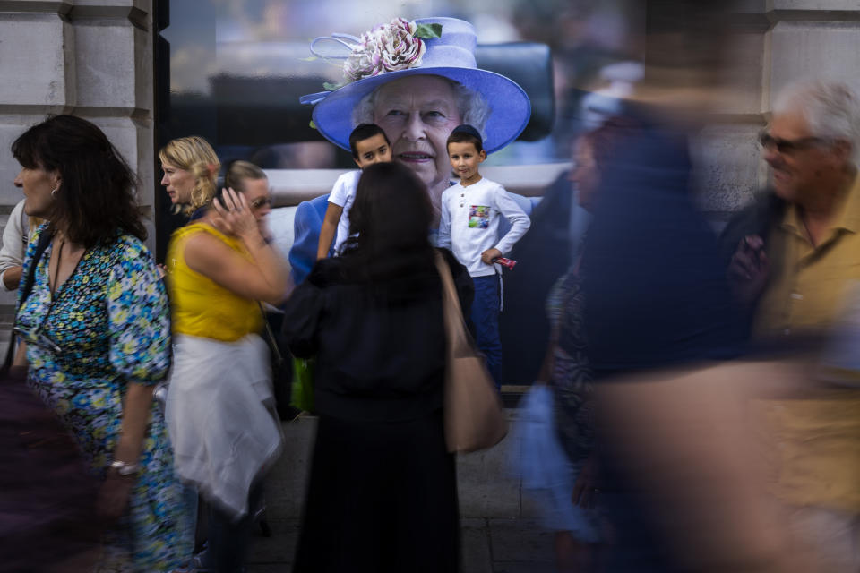 FILE - Pedestrians walk past a portrait of the late Queen Elizabeth II near Buckingham Palace in London, Sunday, Sept. 11, 2022. On morning television, the moment was singularly somber — the departure of the hearse bearing the flag-draped coffin of Queen Elizabeth II. But at the very same hour, as fans in shorts and Ray-Bans streamed into London's Oval stadium for a long-anticipated cricket match, you wouldn't have guessed the country was preparing for the most royal of funerals. (AP Photo/Emilio Morenatti, File)