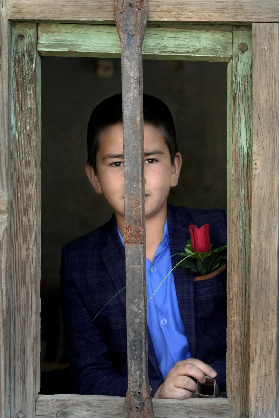 An Afghan student stands behind the classroom window after taking a rose on the first day of school after Tuesday's explosion in front of his school, in Kabul, Afghanistan, Saturday, April 23, 2022. On Saturday, the Abdul Rahim Shaheed School, which was among the IS-K targets in the Tuesday attacks, re-opened. The school's principal handed each student a pen and a flower as they began classes on Saturday. (AP Photo/Ebrahim Noroozi)